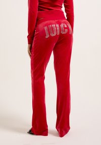 Rote Samthosen mit einem taillierten Bund, versehen mit einem Strass-Design "JUICY" auf der Rückseite, schmal zulaufenden Beinen und einer glatten Textur.