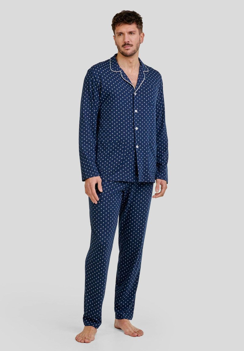 Conjunto de pijama azul marino hecho de una tela suave, que presenta lunares blancos, una camisa de botones con cuello y pantalones a juego con cinturilla elástica.
