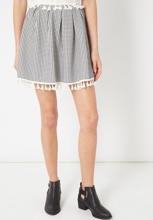 Falda de cuadros en blanco y negro con un diseño plisado, terminada con un borde de borlas blancas. Combinada con botas de tobillo negras con hebilla.