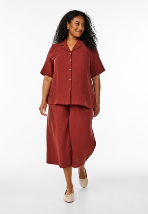 Rust-colored two-piece outfit featuring a short-sleeve button-up shirt and wide-leg pants made of textured fabric. Simple design with brass buttons.