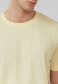 Jasnożółta bawełniana koszulka z okrągłym dekoltem. Posiada małe, haftowane logo na piersi oraz krótkie rękawy. Gładka tekstura.