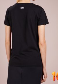 Black cotton t-shirt with short sleeves. Features a small white logo printed at the back, simple design, and a classic crew neckline.