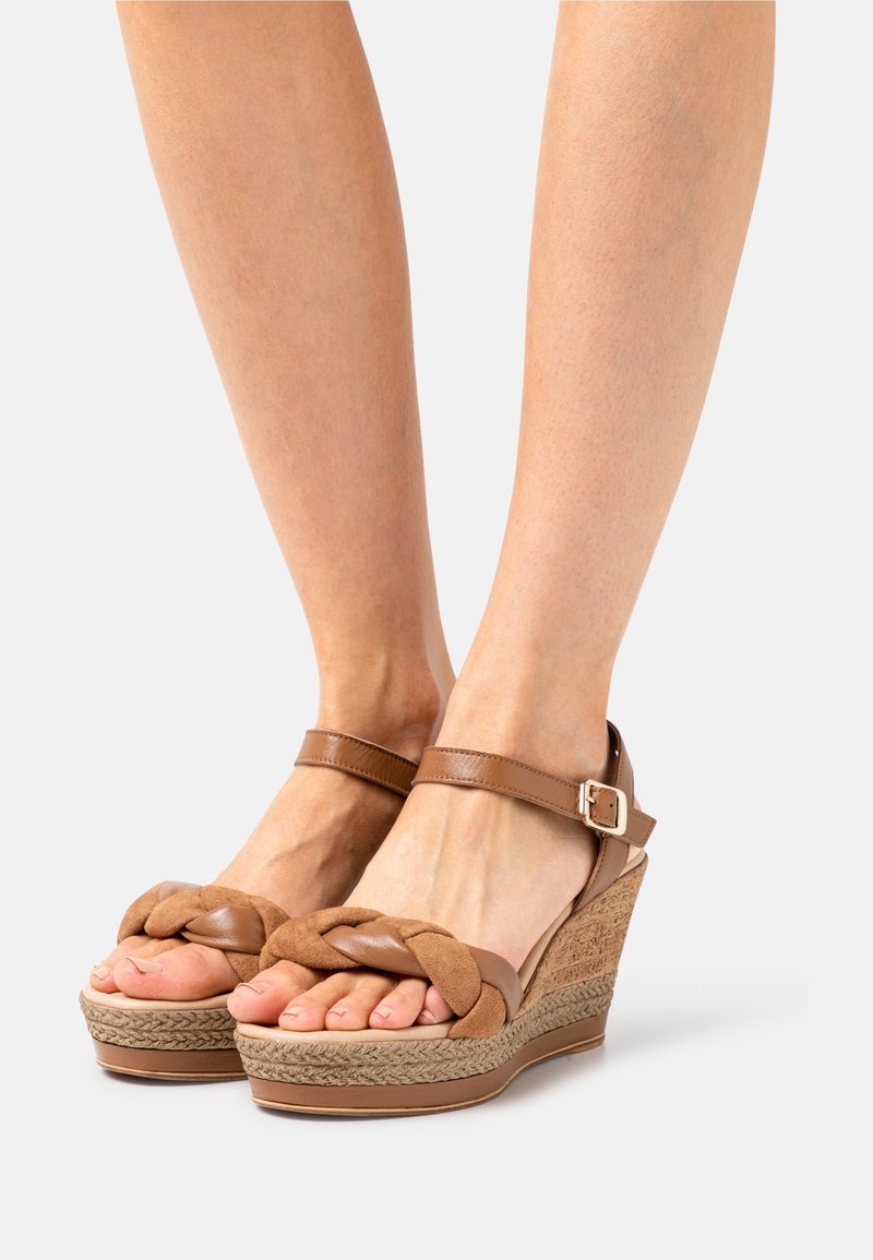 Sandales compensées marron avec un design tressé à l'avant, des sangles en cuir, une boucle à la cheville et une semelle en corde texturée.