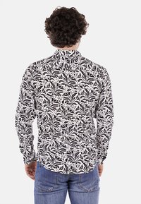 Camicia manica lunga con motivo floreale bianco e nero, dotata di un colletto con bottoni e orlo curvo. Tessuto misto cotone.