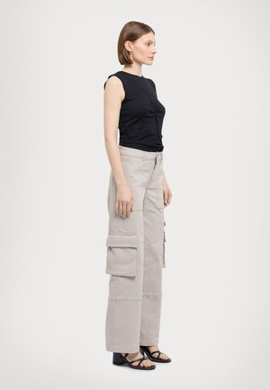 Top nero senza maniche con raccoglimento frontale, abbinato a pantaloni cargo beige chiaro con più tasche e design a gamba dritta. Sandali neri con tacco.