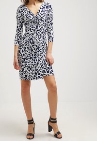 Knee-length dress in navy and white floral pattern, featuring a V-neck and three-quarter sleeves. Paired with black high-heeled sandals.