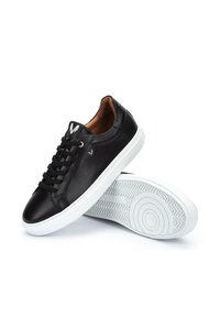 Sneaker in pelle nera con finitura liscia, suole in gomma bianca e lacci neri. Presenta un piccolo logo sulla linguetta e una suola decorata.