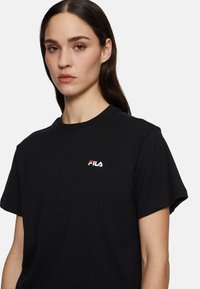 Zwarte katoenen t-shirt met ronde hals en korte mouwen, voorzien van een klein rood en wit Fila-logo op de linkerkant van de borst.