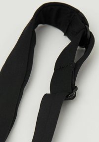 Czarny elastyczny pasek, z zaokrąglonym końcem i regulowanym okrągłym elementem z materiału. Gładka tekstura o stałej szerokości w całej długości.