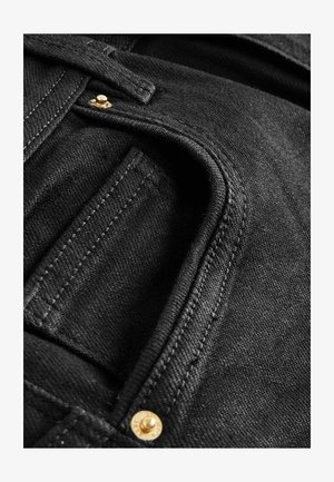 Svart denimtyg har en framträdande fickdetalj med synlig sömnad och en gyllene knapp. Texturen är slät med en lätt lyster.