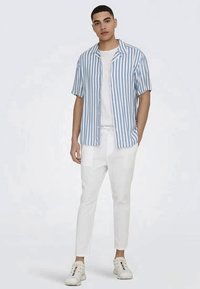 Short-sleeve, button-up shirt in light blue and white stripes. Paired with white tapered pants and white sneakers. Smooth texture.
