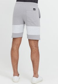 Shorts de sport gris avec des détails en pince légèrement gris, taille élastique et poche arrière. Le tissu semble doux et légèrement texturé.