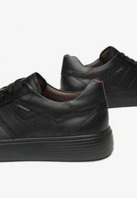 Sneaker in pelle nera con superficie testurizzata, punta tondeggiante e interno marrone a contrasto. Presenta dettagli perforati e suola in gomma robusta.