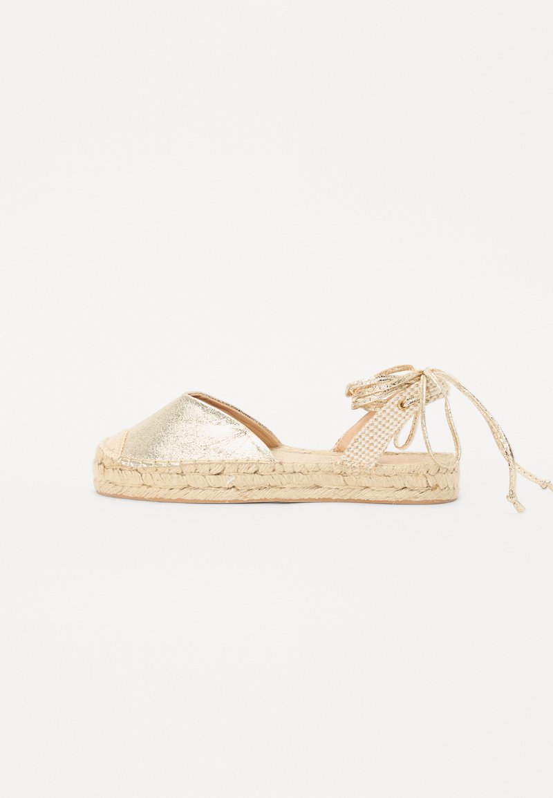 Gold metallic espadrille with a woven jute sole and ankle tie. Features a rounded toe and textured fabric finish.