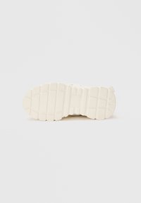 Semelle de sneaker blanche avec un design texturé et rainuré. Présente des crans prononcés et une pointe arrondie pour une meilleure adhérence et une stabilité accrue.