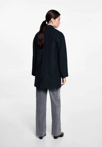 Lång marinblå kappa med vertikala randningar, skräddarsydd design, texturerad tyg och rak skärning. Kombinationen med grå vida jeans.