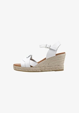 Sandalia blanca de cuña con suela de yute trenzado, correas entrecruzadas y una correa de tobillo con un hebilla de metal. Parte superior de piel suave.