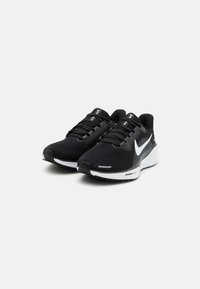 Zapatos deportivos negros con una parte superior de malla transpirable, acentos blancos, suela acolchada y sistema de cordones tradicional.