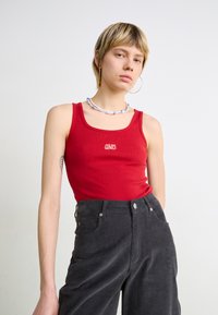 Top de alças vermelho canelado com um pequeno logótipo bordado, combinado com calças de veludo cotelê cinza-escuro de cintura alta, com bolsos frontais e fecho com botão.
