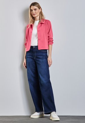 Giacca button-up rosa, t-shirt bianca, jeans a gamba larga blu scuro e sneakers bianche. Tessuti morbidi, vestibilità rilassata e stile casual.