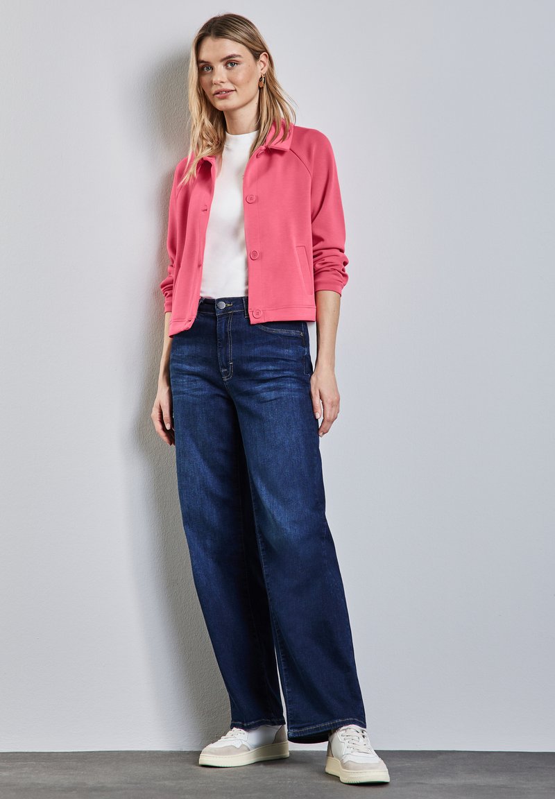 Rosafärgad skjortjacka med knappar, vit t-shirt, mörkblå vida jeans och vita sneakers. Släta tyger, avslappnad passform och casual stil.
