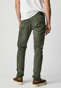 Green denim jeans featuring a slim fit, back pockets with contrasting stitching, and a black brand label on the waistband.