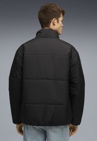 Sort pufferjakke med høj krave og quiltet design. Lavet af glat stof, med en løs pasform og elastisk kant.