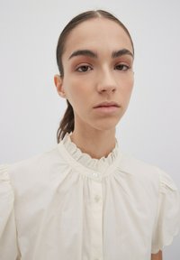 Helle cremefarbene Bluse mit einem Rüschenkragen und kurzen Puffärmeln, ausgestattet mit einer durchgehenden Knopfleiste und glattem, leichtem Stoff.