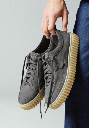 Sneakers in suede grigio con superficie testurizzata, punta rotonda e suola in gomma traslucida e spessa. Presentano lacci arrotondati e un'etichetta di marca sul lato.