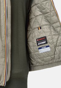 Giacca trapuntata verde con fodera interna grigio chiaro, dotata di etichette Primaloft e K-Way. Cerniera con accento multicolore e polsini in maglia.