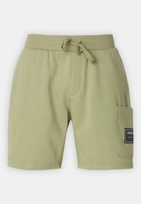 Shorts en sweats verts clairs avec un bandeau à cordon de serrage, une poche latérale et un patch de marque sur la poche droite. Tissu en coton doux.