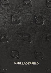 Juodas odinis pinigine su iškiliais Karl Lagerfeld logotipais, sidabriniu ženklu, tekstūruotu paviršiumi ir kompaktiška stačiakampio forma.