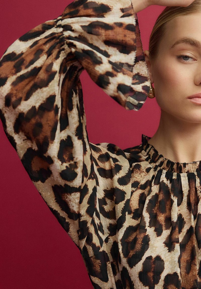 Blůza s leopardím potiskem vyrobená z lehkého materiálu, s volnými rukávy, nařaseným výstřihem a složitými texturálními detaily.