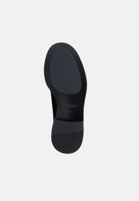 Μαύρη σόλα παπουτσιού από καουτσούκ με λεία υφή, οβάλ περιοχή τακουνιού και οριζόντιες ραβδώσεις για κράτημα. Παρουσιάζει σφραγισμένο λογότυπο και λεπτομέρεια μεγέθους.