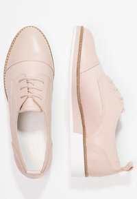 Scarpe in ecopelle rosa chiaro con punta arrotondata, design con lacci, dettagli beige e suola in gomma bianca. Decorazioni testurizzate sui lati.