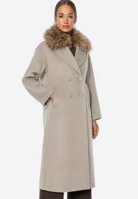 Beige, doppelt geknöpfter Mantel mit einem strukturierten Kunstfellkragen, langen Ärmeln und seitlichen Taschen, gefertigt aus einem weichen, wollähnlichen Material.