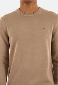 Maglione beige lavorato a maglia con colletto rotondo a coste e tessuto testurizzato, caratterizzato da un piccolo logo del marchio sul petto.
