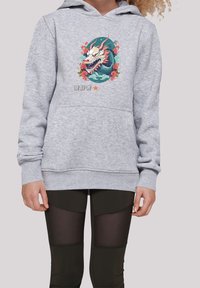 Sudadera gris con un diseño gráfico de dragón, acentos florales, bolsillo frontal, puños y dobladillo acanalados. Combinada con leggings negros que presentan paneles de malla.