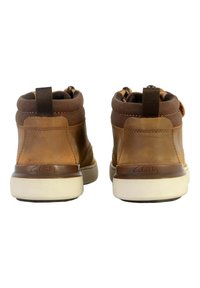 Botas de tobillo de cuero marrón con un suave collar de tela marrón, suela de goma blanca y lazos en la parte trasera para facilitar el uso. Marca Clarks visible.