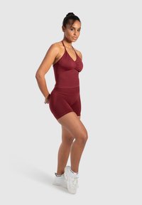 Bourgondische sportoutfit met een aansluitend tanktop met een ronde halslijn en bijpassende hoge shorts, gecombineerd met witte sneakers.