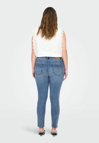 Lengvas baltas nėriniuotas švarkelis su banguotais kraštais, derinamas su tiksliomis mėlynomis džinsais. Džinsai turi galinius kišenes ir odinį ženkliuką.