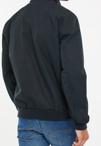 Black nylon bomber jacket with a stand collar, elastic cuffs, and waistband. Smooth texture; plain design, showcasing a minimalist style.