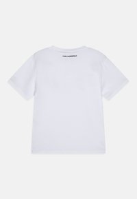 Camiseta de algodón blanca de manga corta, con cuello redondo y "KARL LAGERFELD" impreso en negro en la parte superior de la espalda. Textura suave.