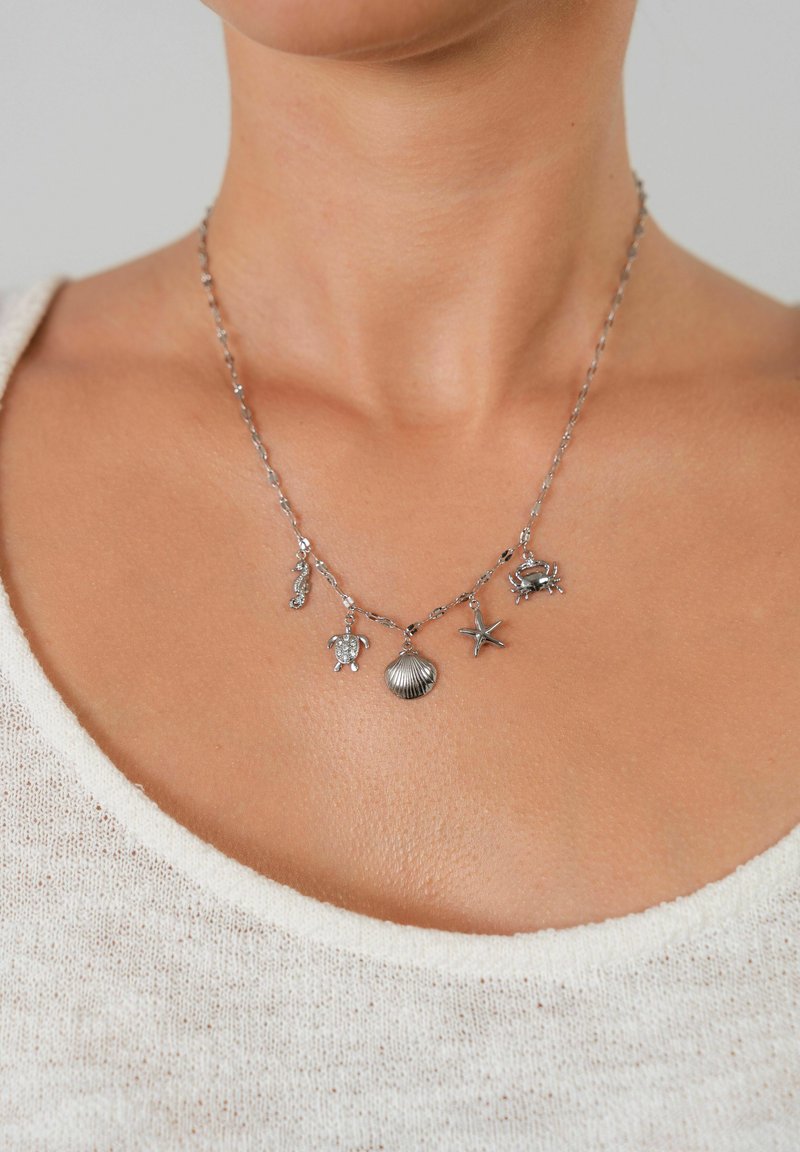 Die silberne Halskette verfügt über fünf marine-inspirierte Anhänger: ein Seepferdchen, eine Schildkröte, eine Muschel, einen Seeigel und einen Krebs, die alle mit filigranen Details gestaltet sind.