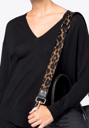 Personne portant un pull noir à col en V tenant un sac à main texturé noir avec une bandoulière amovible imprimée léopard sur l'épaule.