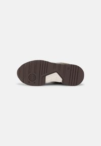 Schuhsohle aus braunem Gummi, strukturiert für besseren Halt. Verfügt über einen weißen Zwischensohlenbereich und ein kreisförmiges Muster in der Nähe der Ferse.