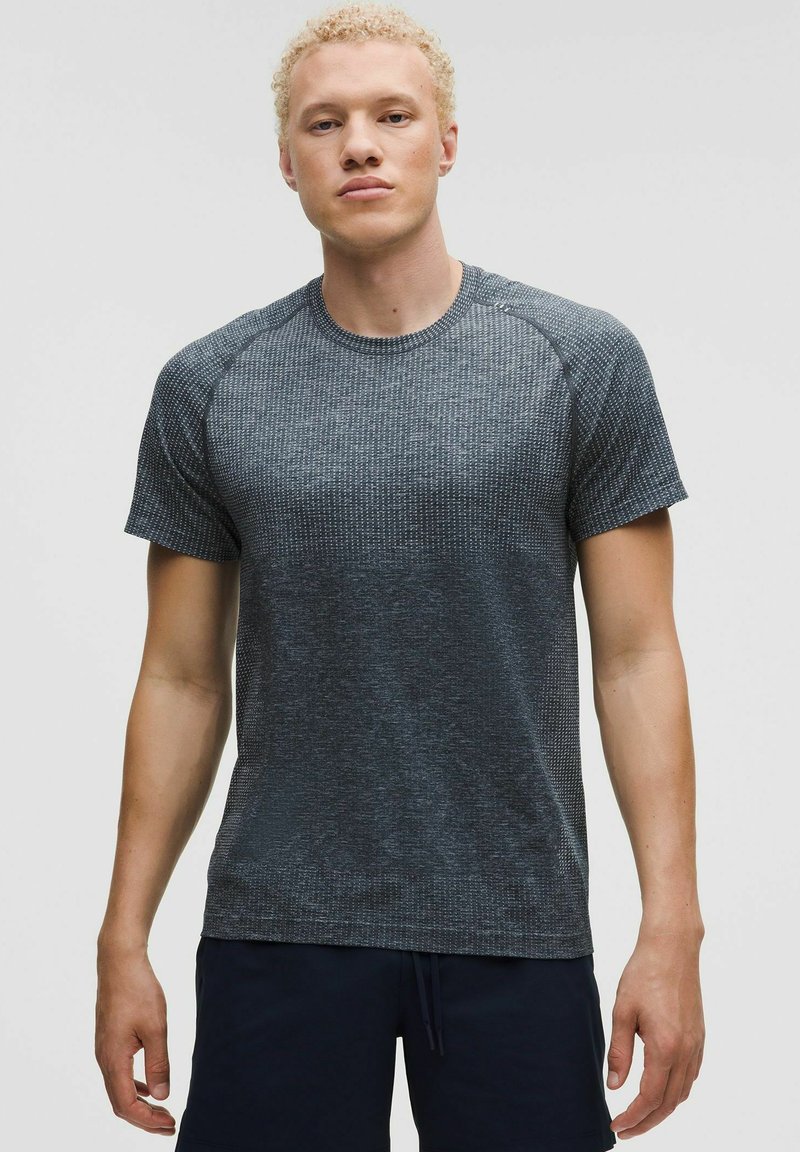 Szary, teksturowany t-shirt z krótkim rękawem, okrągłym dekoltem i rękawami raglanowymi, wykonany z elastycznego materiału. Brak widocznych logo lub wzorów.