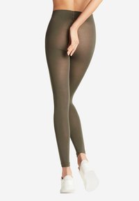 Olijfgroene legging met ribbelstructuur, hoge tailleband en een aangesloten silhouet. Gepaard met witte instap schoenen.