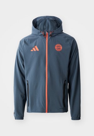 Férfi szélálló dzseki, kék anyag, narancssárga részletekkel, állítható kapucni, elöl cipzár, két oldalsó zseb, a Bayern München logójával.