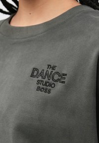 Γκρι φούτερ με ριμπ ζιβάγκο και κεντημένο κείμενο: «THE DANCE STUDIO BOSS» σε μαύρο, με λείο και υφασμάτινο ύφασμα.